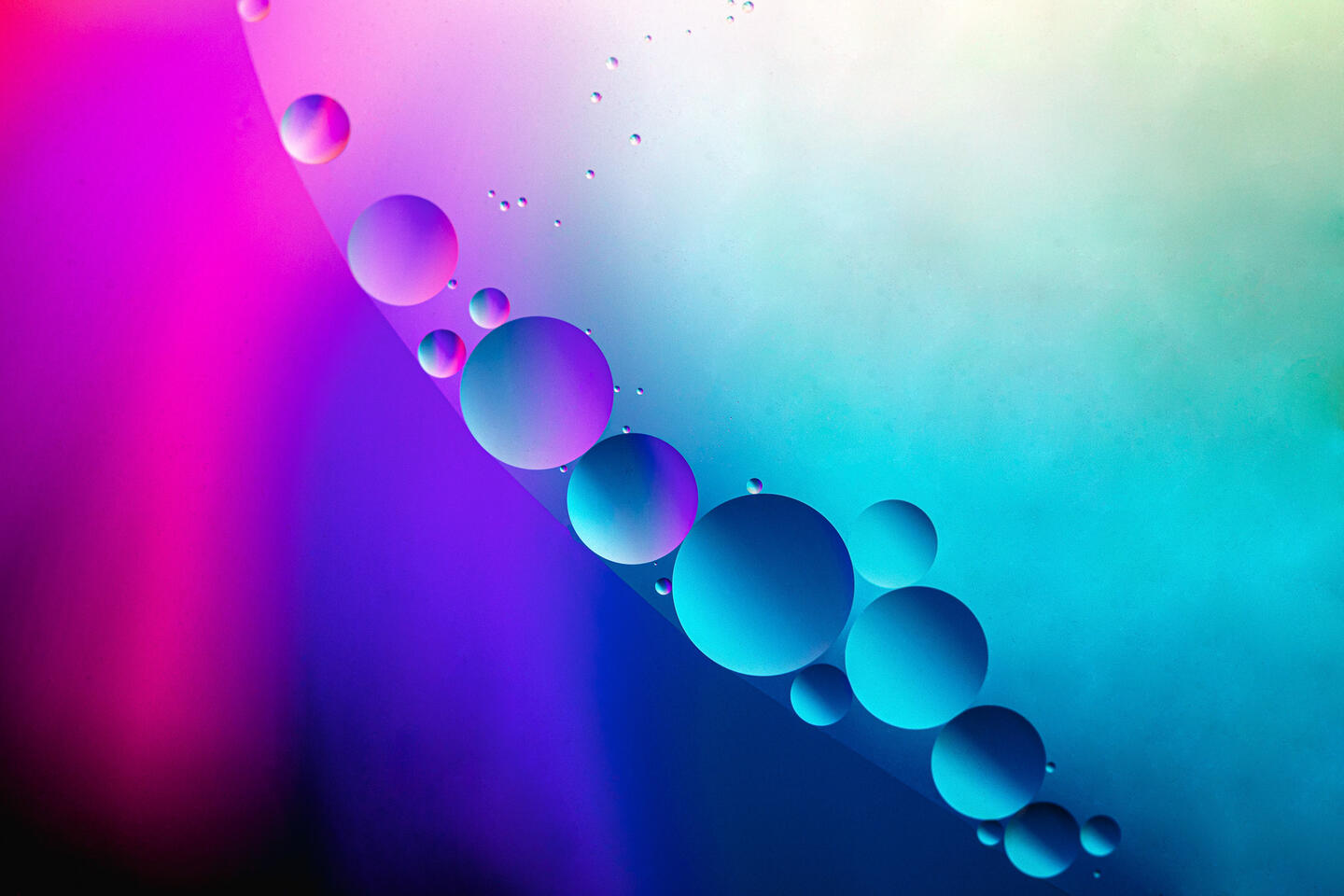 Close-up of oil droplets in a diagonal line with gradients of magenta, blue, and cyan light.